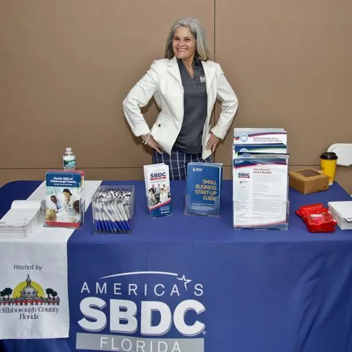A woman stands behind a table displaying small-business guides and resources.