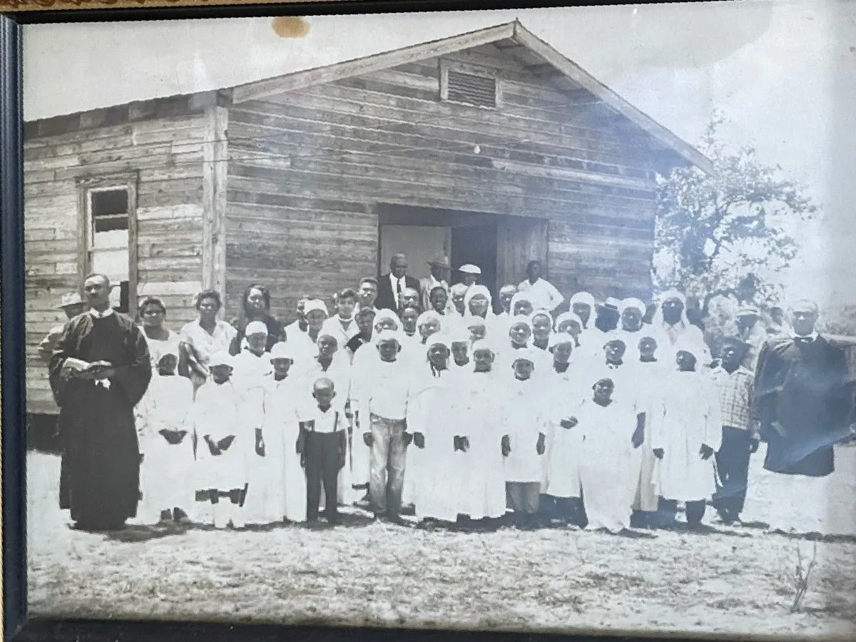 Historic community group gathered outside a weathered wooden building.