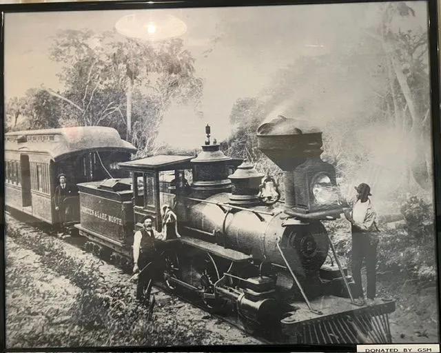Historic photograph of a steam train with passengers and railway workers beside the tracks.