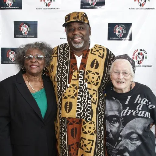 Three community members pose together, with the person in the center wearing a patterned cultural garment.